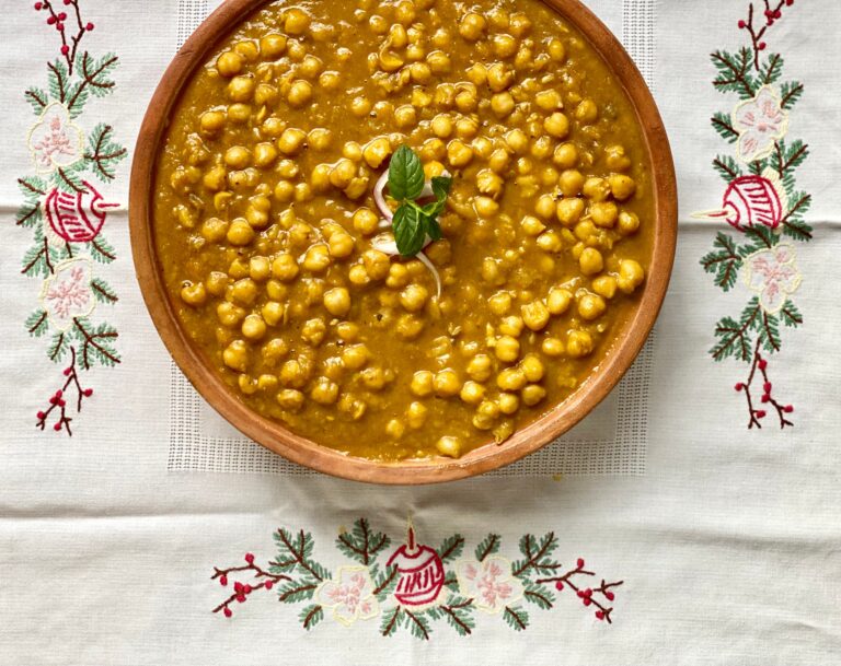 An overhead view of a clay bowl filled with cooked chana daal on a white embroidered cloth