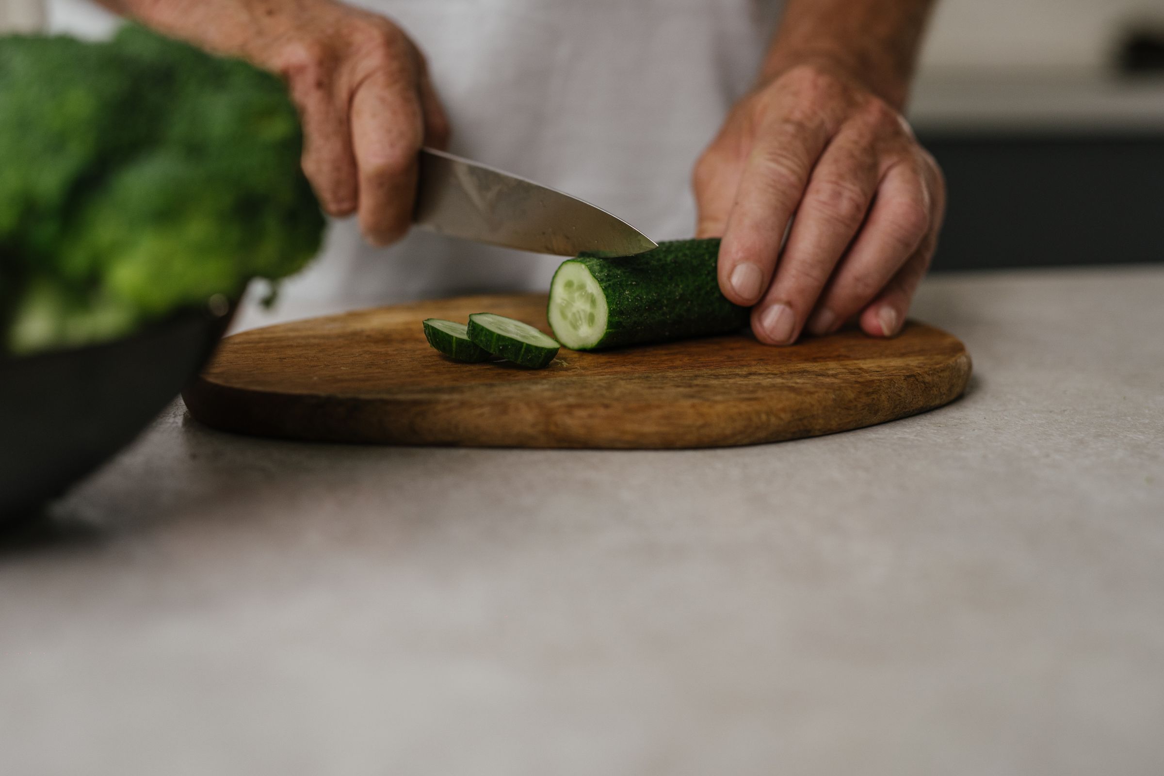 Slicing fresh green cucumber on a wooden chopping board for a kidney disease diet